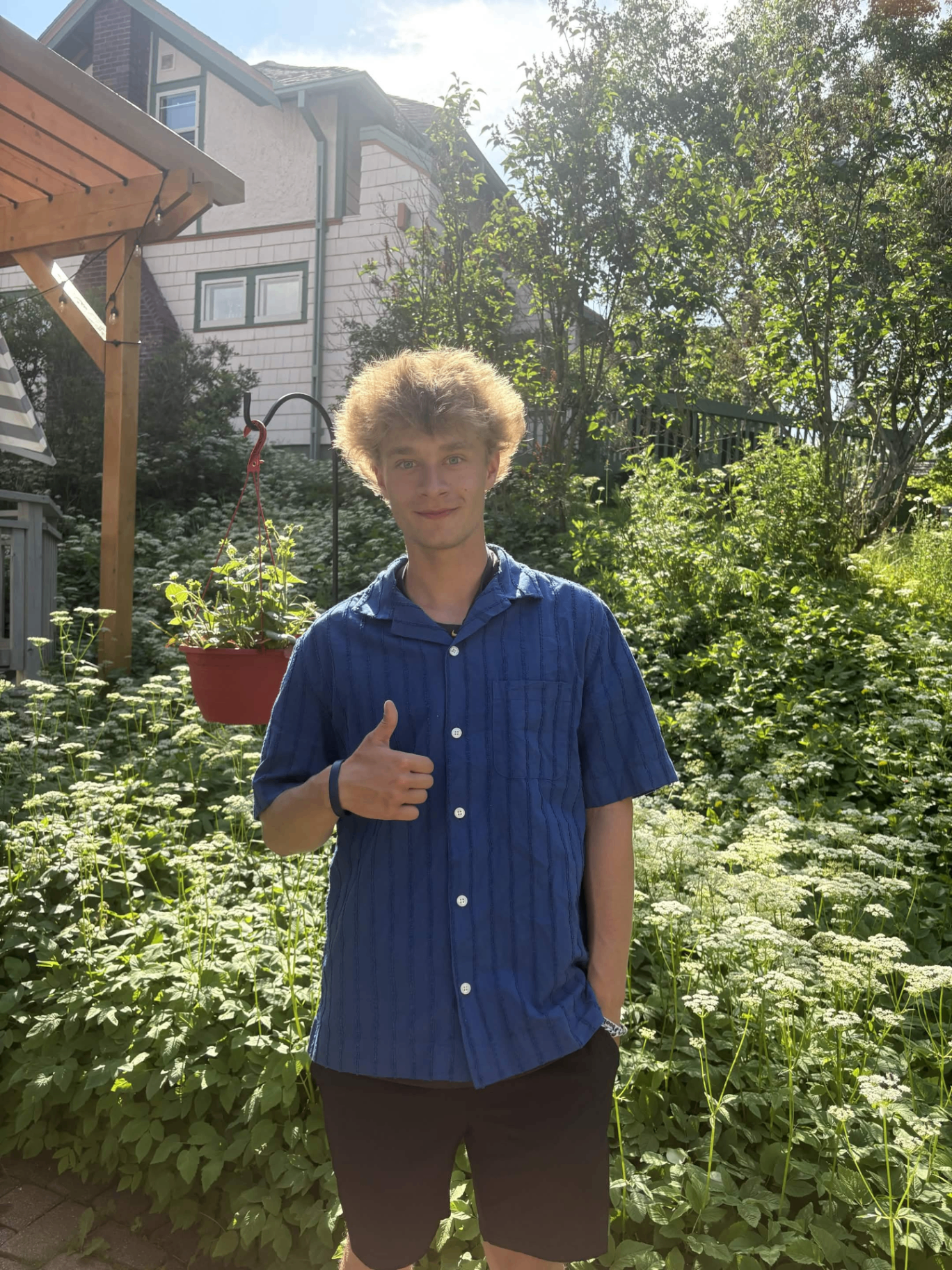 Peyton Hansen, owner of Lake Superior Lawncare, smiling and giving a thumbs-up in a lush green garden in Duluth, Minnesota